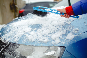Woman wipes snow machine using winter brush, blue background