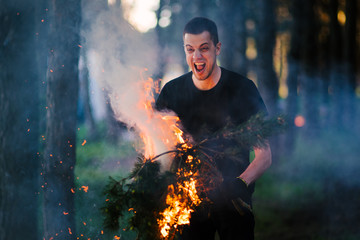 Man stands with torches on the background of the forest. An image of man holding burning stick while moving outdoors, surviving in the wild