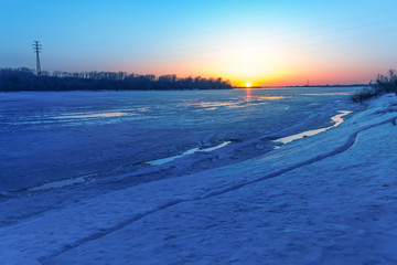 Beautiful sunset over a frozen river. The river is bound by ice. Spring landscape.