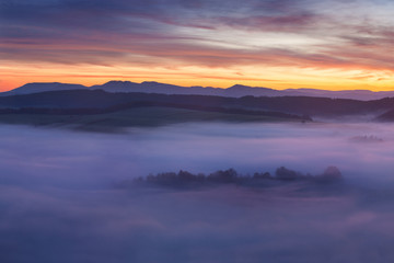 Sunset Over Misty Landscape Scenic View Of Foggy Morning Sky With Rising Sun Above dreamy Forest. Mountain range with visible silhouettes through the morning colorful fog  Beautiful background concept