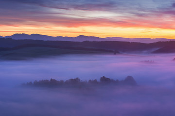 Naklejka na ściany i meble Sunset Over Misty Landscape Scenic View Of Foggy Morning Sky With Rising Sun Above dreamy Forest. Mountain range with visible silhouettes through the morning colorful fog Beautiful background concept
