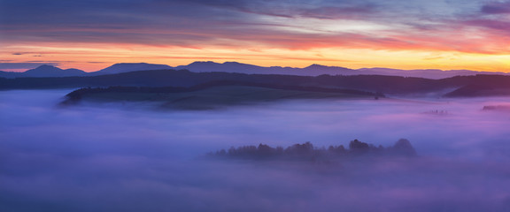 Sunset Over Misty Landscape Scenic View Of Foggy Morning Sky With Rising Sun Above dreamy Forest. Mountain range with visible silhouettes through the morning colorful fog  Beautiful background concept