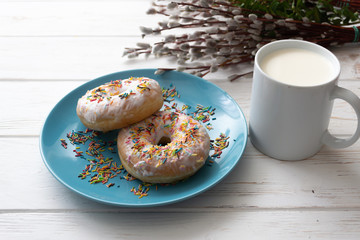Donuts on a blue plate with a cup of milk on a white wooden background