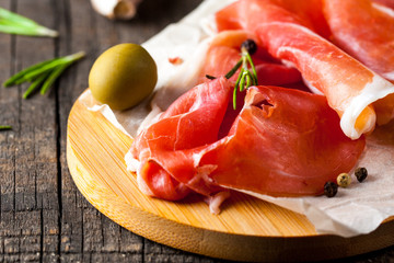 Closeup of thin slices of prosciutto with mixed olives and paprika on wooden cutting board