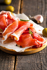 Closeup of thin slices of prosciutto with mixed olives and paprika on wooden cutting board