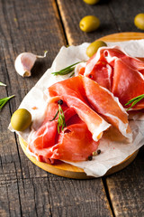 Closeup of thin slices of prosciutto with mixed olives and paprika on wooden cutting board