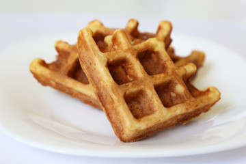 Belgian waffles in white plate. Healthy breakfast close up, pieces of freshly baked classic wafer