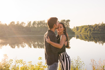 Fototapeta na wymiar Relationship, love and nature concept - Attractive woman and handsome man hugging and kissing over water background
