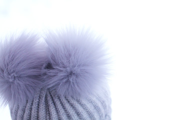 gray fur pompons on a woolly hat on a winter background