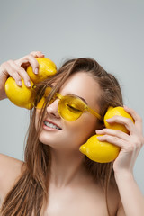 Joyful young woman in yellow sunglasses holding lemons near head. Healthy Lifestyle.