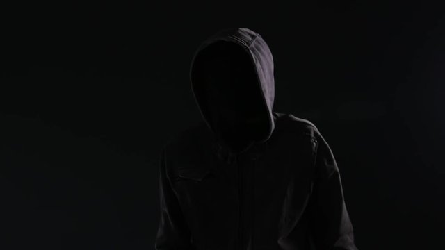 Unrecognizable hooded maniac stalker gesturing finger on lips or shh sign to silence the victim of his crime act