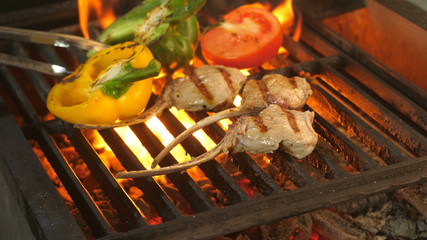 steak on the bone grilled, the chef moves the forceps with pincers, the pepper is cut in half and half a tomato on the side away from the open fire