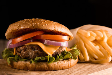 Home made hamburger with beef, onion, tomato, lettuce and cheese. Fresh burger close up on wooden rustic table with potato fries, beer and chips. Cheeseburger.