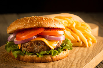 Home made hamburger with beef, onion, tomato, lettuce and cheese. Fresh burger close up on wooden rustic table with potato fries, beer and chips. Cheeseburger.