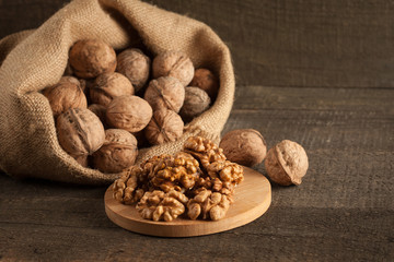 Walnut kernels in sack and whole walnuts on rustic old wood.