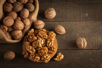 Walnut kernels in sack and whole walnuts on rustic old wood.