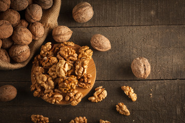 Walnut kernels in sack and whole walnuts on rustic old wood.