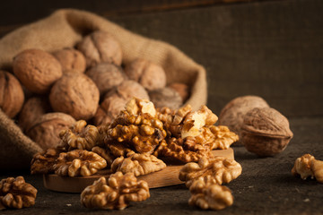 Walnut kernels in sack and whole walnuts on rustic old wood.