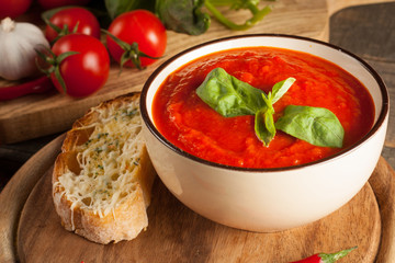 Fresh, healthy tomato soup with basil, pepper, garlic, tomatoes and bread on wooden background. Spanish gazpacho soup.