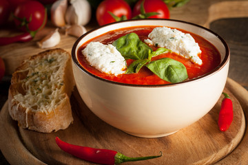 Fresh, healthy tomato soup with basil, pepper, garlic, tomatoes and bread on wooden background. Spanish gazpacho soup.