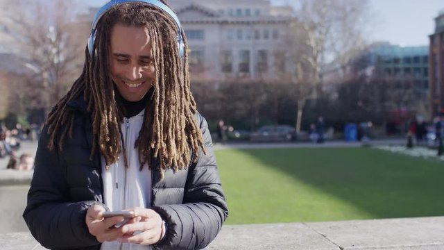Portrait of stylish young man wearing headphones using his phone outdoors