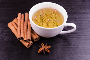 A cup of green tea with flowers, a sticks of cinnamon and anise