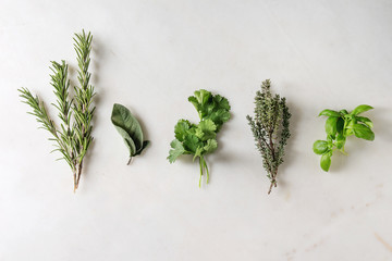 Variety of fresh kitchen herbs with scissors in row over white marble background. Flat lay, space....