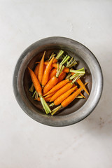 Young mini carrot in water in vintage metal bowl over white marble background. Flat lay, space. Cooking concept, food background.