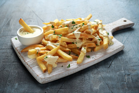 Homemade Baked Potato Fries with cheese sauce on white wooden board