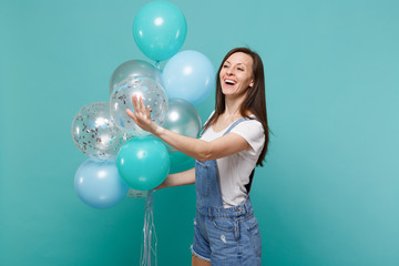 Fototapeta premium Smiling woman looking aside, waving greeting with hand as notices someone celebrating hold colorful air balloons isolated on blue turquoise background. Birthday holiday party, people emotions concept.