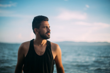 A young man looks at the sunset by the sea. A handsome guy is sitting on the rocks in the sea at sunset. Portrait