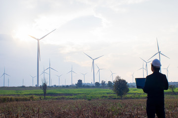 Engineer standing and playing laptop with wind turbine.