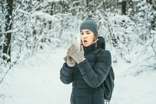 Beautiful woman dressed in a black winter jacket with mobile phone. Snow landscape background behind