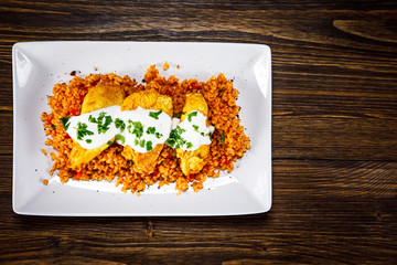 Grilled chicken meat with groats and vegetables on wooden table