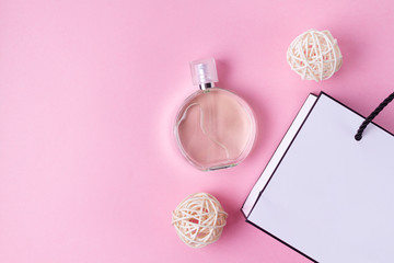 Bottle of favorite women's perfume and a gift paper bag on a pink background. Top view. Copy space