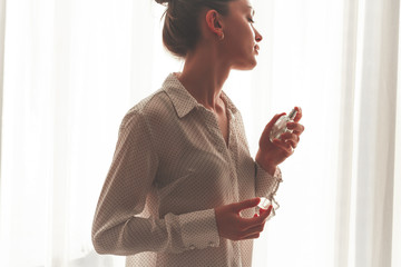 Stylish young beautiful woman in blouse spraying favorite perfume. Fashion, beauty and style