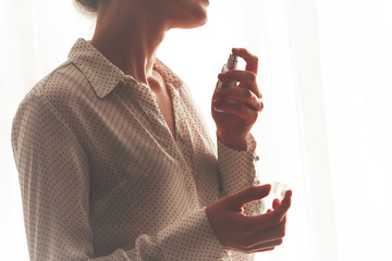 Stylish woman in blouse spraying a bottle of favorite perfume close up at home. Fashion, beauty and...