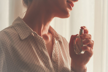 Stylish woman in blouse spraying a bottle of favorite perfume close up at home. Fashion, beauty and...