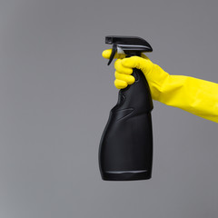 A hand in a rubber glove holds the glass cleaner in a spray bottle on a neutral background. The concept of bright spring, spring cleaning.
