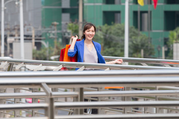 Young woman is walking and hold lot of colorful shopping bags in her hand. She is very happy and enjoyed shopping on sales period. Holiday shopping concept.