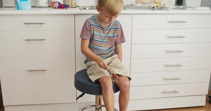 Child patient in pediatric office playing with reflex hammer. Little boy waiting on doctor in exam room. Slow motion 4k