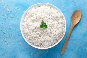 Bowl with white boiled rice with green fresh parsley for delicious healthy lunch on a blue background. Cereal food and dishes. Top view