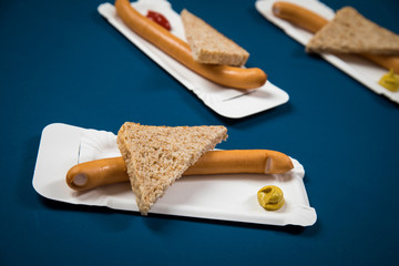 Fototapeta premium Wiener Würstchen mit Vollkorn Brot Scheibe auf Einweg Pappteller mit Senf und Ketchup auf Hintergrund Blau