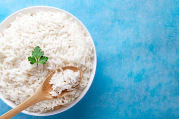 Bowl with boiled rice with green fresh parsley for delicious healthy lunch on a blue background. Cereal food and dishes. Top view and copy space