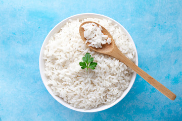 Bowl with boiled rice with green fresh parsley for delicious healthy lunch on a blue background. Cereal food and dishes. Top view