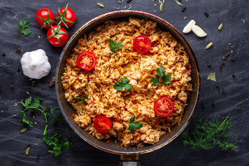 Homemade delicious pilaf with chicken, fresh parsley and ripe vegetables in a pan for lunch on a...
