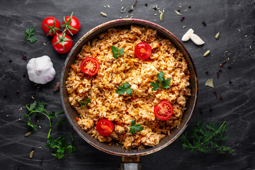 Homemade delicious pilaf with chicken, fresh parsley and ripe vegetables in a pan for lunch on a dark background. Top view