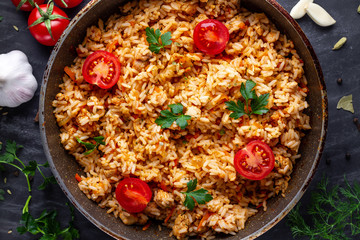 Homemade delicious pilaf with chicken, fresh parsley and ripe vegetables in a pan on a dark background close up. Top view