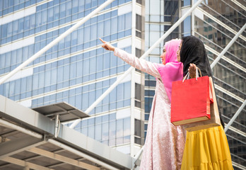 Fototapeta na wymiar Two Arab women are carrying colorful shopping back. Back of middle east girls enjoyed buying stuffs on sales for their vacation with good friend. Holiday shopping concept.