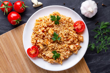Plate of homemade delicious pilaf with chicken, fresh parsley and ripe vegetables for lunch. Top view